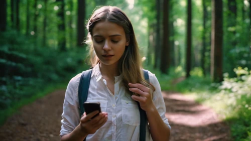 woman holding a smartphone,online path travel,girl with tree,girl in a long,forest background,using phone,woman walking,music on your smartphone,girl walking away,social media addiction,the app on phone,people in nature,travel woman,orienteering,mobile application,forest walk,landscape background,online course,women in technology,text message,Photography,General,Cinematic
