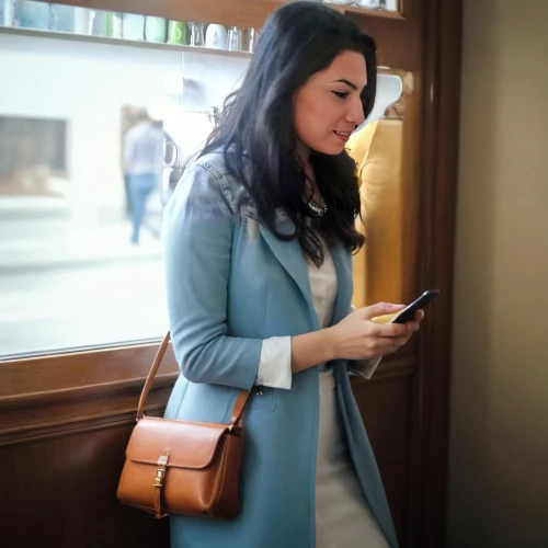 woman holding a smartphone,mobile banking,mobile device,e-book reader case,bussiness woman,menswear for women,handheld device accessory,woman in menswear,the app on phone,conference phone,travel woman,women in technology,businesswoman,sheath dress,mobile tablet,business woman,women fashion,leather suitcase,viewphone,mobile application