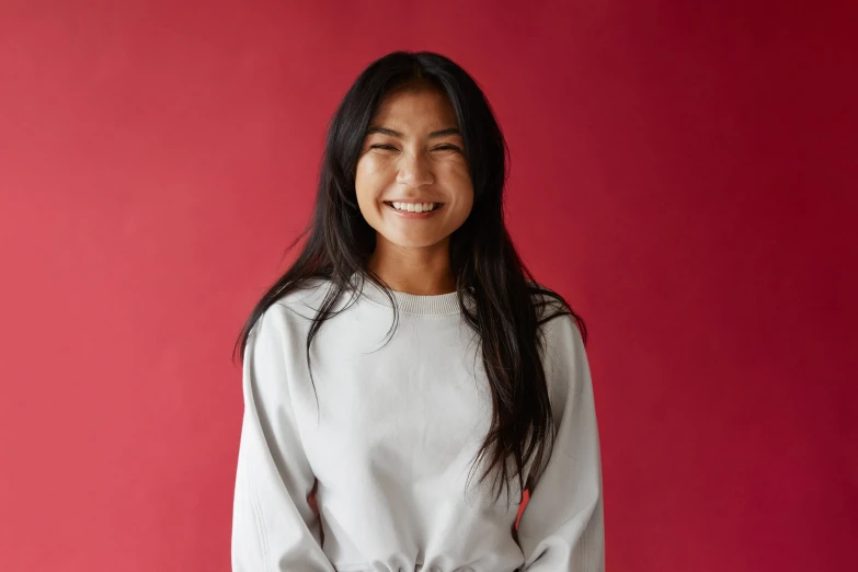 a smiling woman with black pants and a white top is posing for a picture in front of a red wall