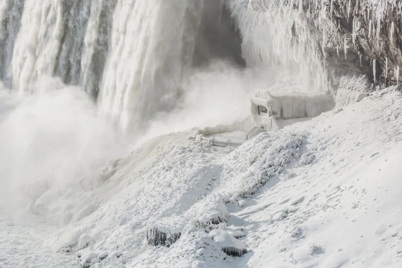 a man walking on snow in front of waterfall