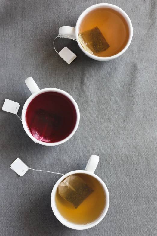 three mugs with different kinds of drinks on the side of a bed