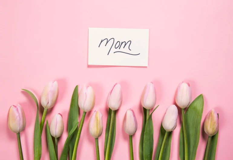 white flowers sitting in front of a pink wall with a note that says mom