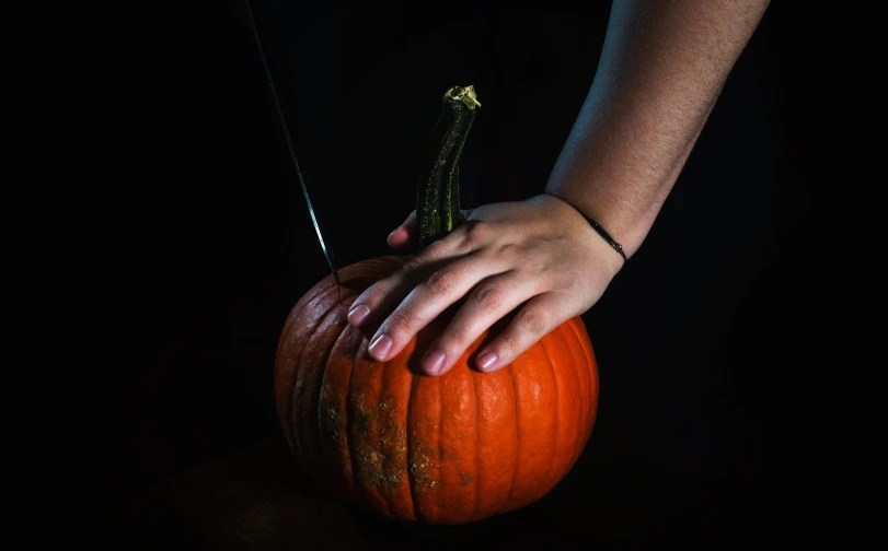 person holds a knife to cut the top of a pumpkin