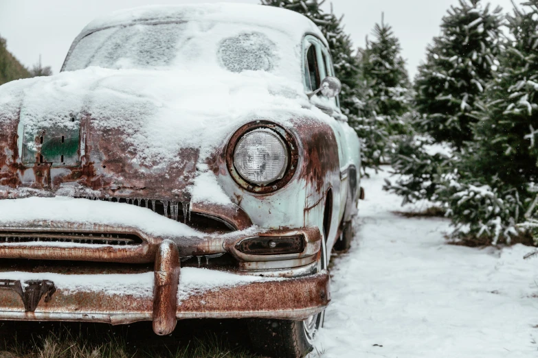 an old rusty car is covered in snow