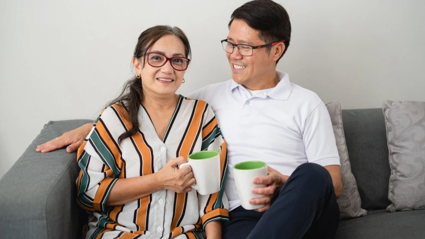 two people sitting on a couch with cups