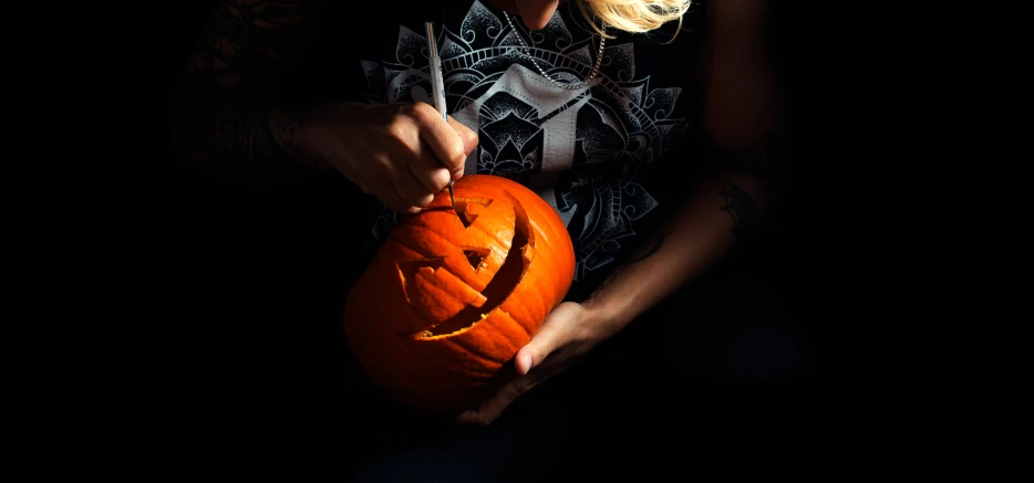 a woman holds an orange carved pumpkin in the dark