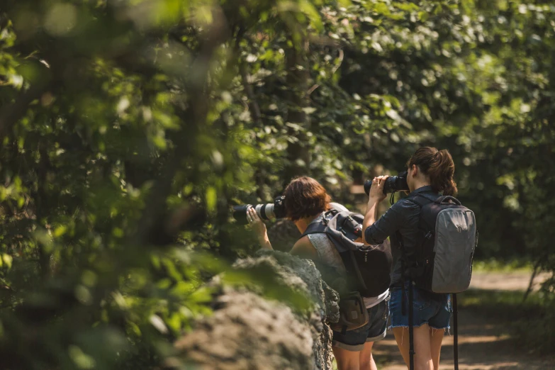 two women taking pictures through leaves on the side of a trail