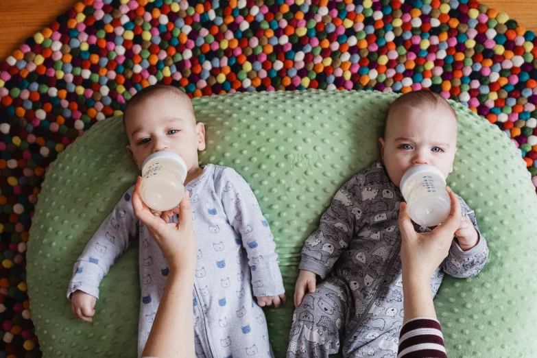 two babys are laying down and one is drinking from bottles