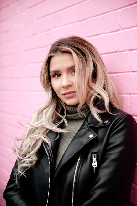 woman with blonde hair posing for the camera in front of a pink wall