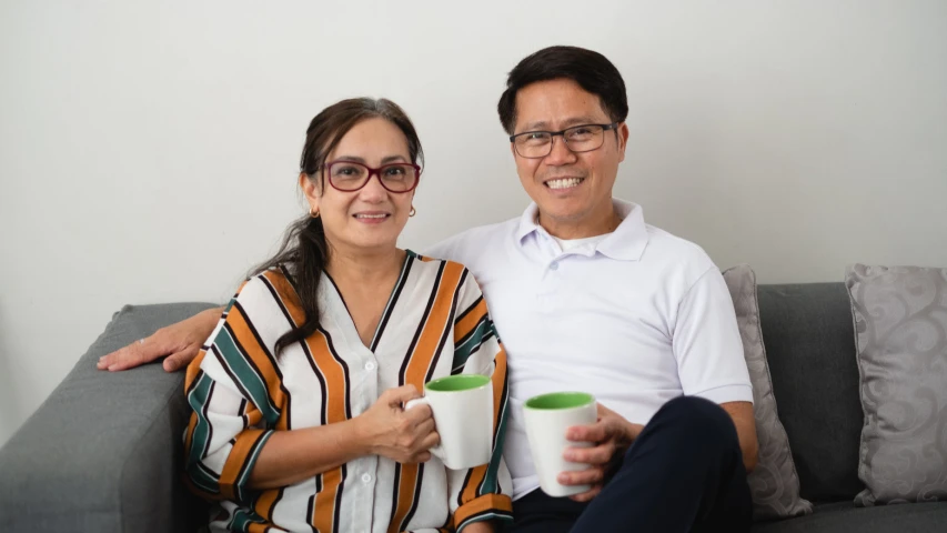 two people sitting on a couch, one holding a cup and smiling