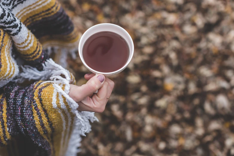 a woman holding a cup of tea outside in the autumn