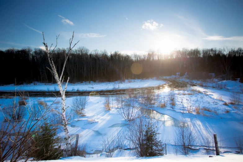 the sun rises above a snowy area with a stream in the foreground