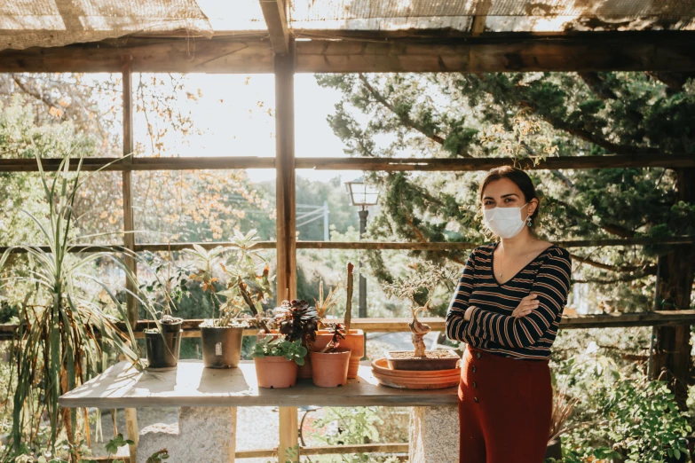 a woman with a face mask on posing next to a table with plants