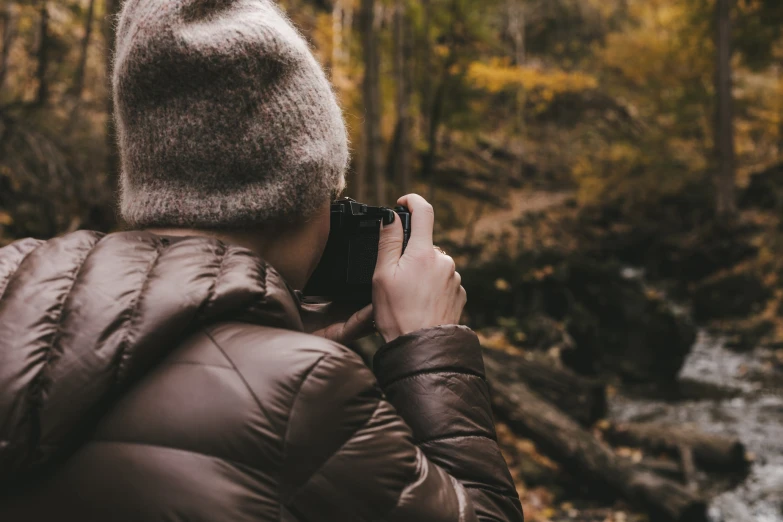 a woman is taking pictures in front of a mountain stream