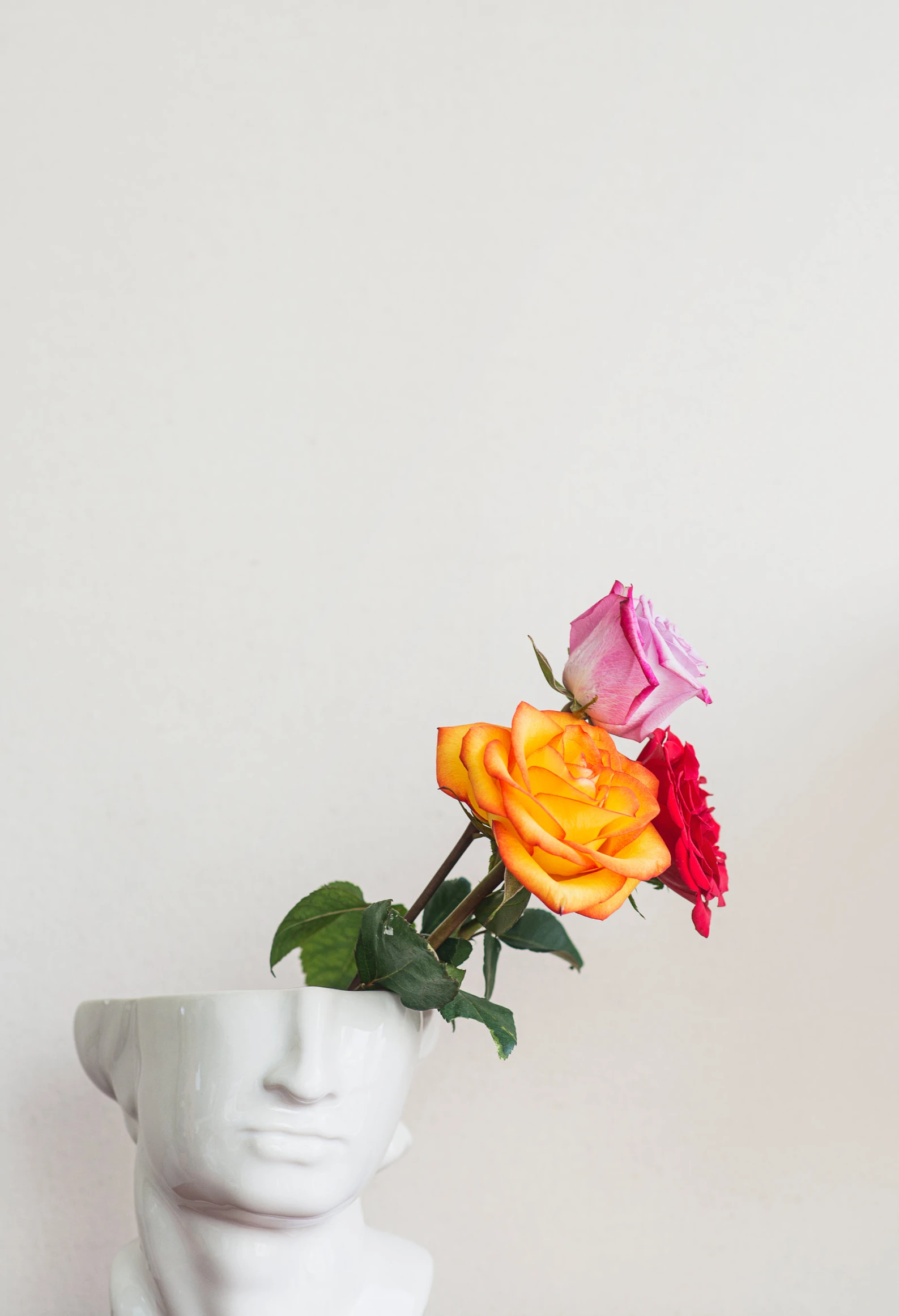 two small flowers sit in the back of a white statue