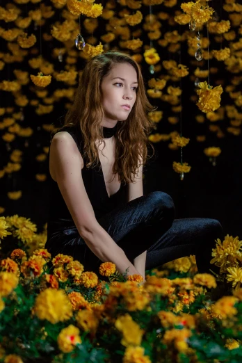 a woman in a black dress is sitting on the ground surrounded by flowers