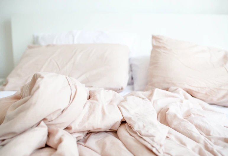 an unmade bed with two pillows and a white blanket