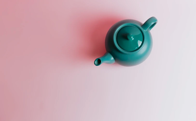 a blue teapot sits atop a pink and white background