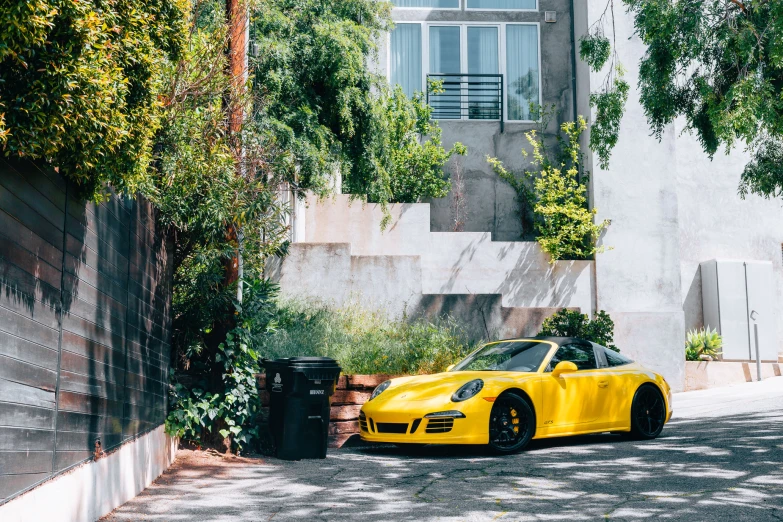 a yellow car parked on the side of a road near some bushes and trees