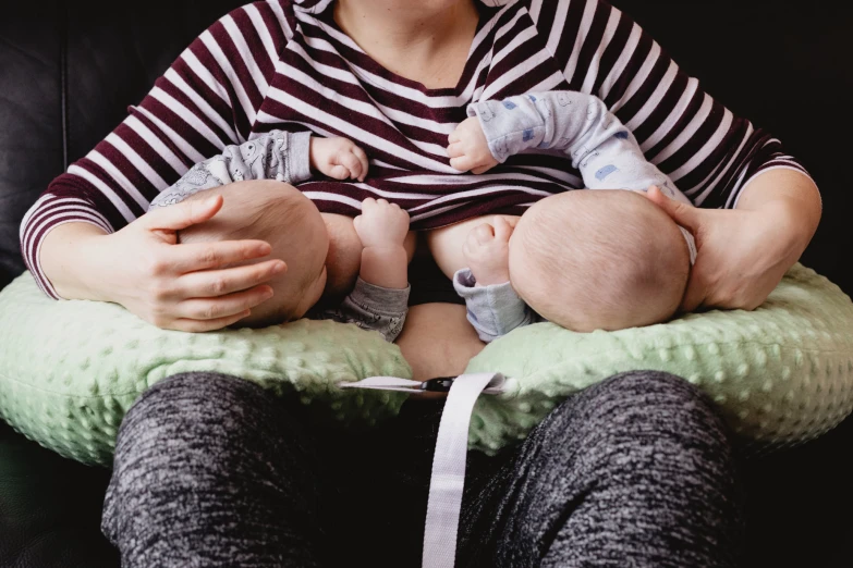 a woman sitting in a black chair holding two babys