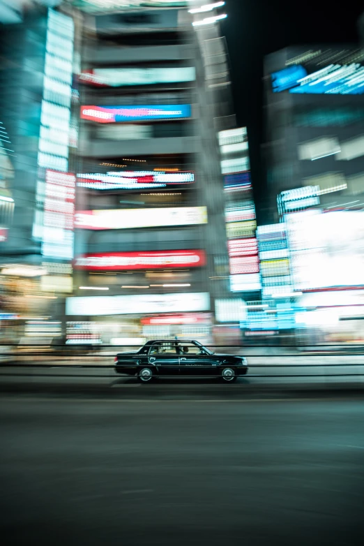 a black car moving down the street with the night lights shining down