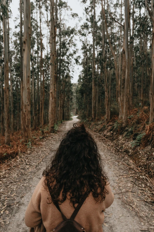a woman is walking down a road through the woods