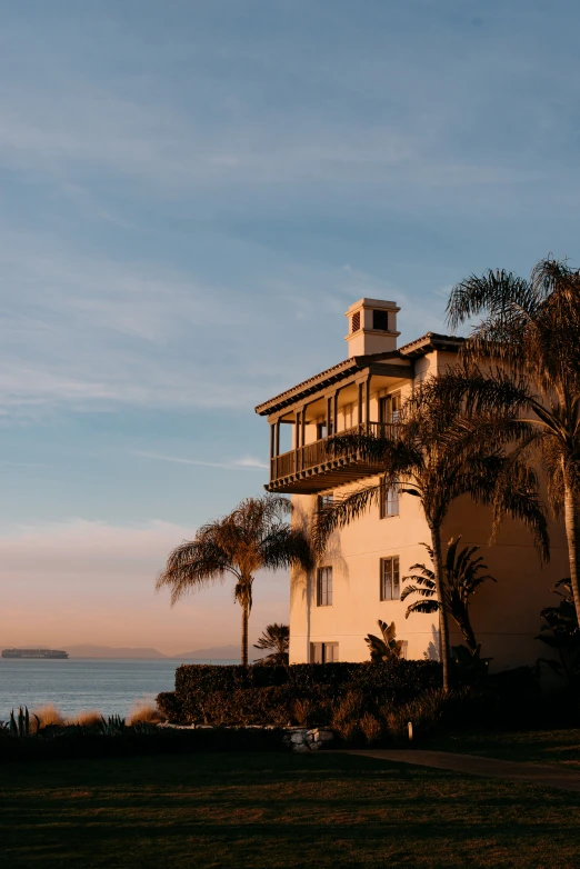 a house next to the ocean with palm trees and water in the background