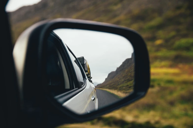 the side view mirror on the back of a car is reflecting a mountain