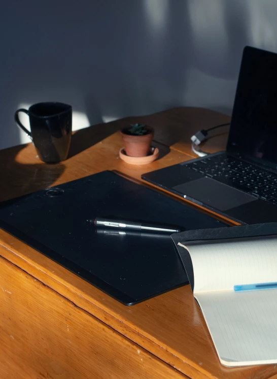 a desk with a laptop, notebook and cup on it