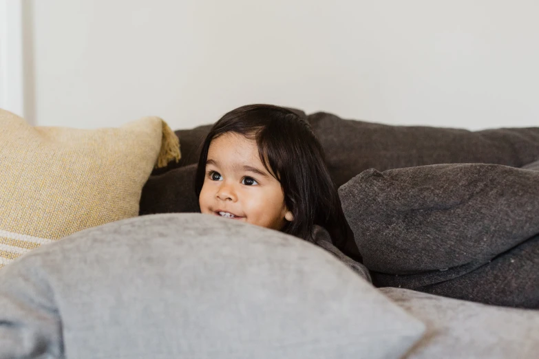 a little girl is hiding in a couch