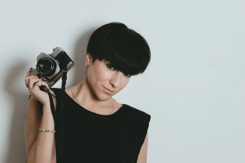 a woman standing against a white wall holding a camera