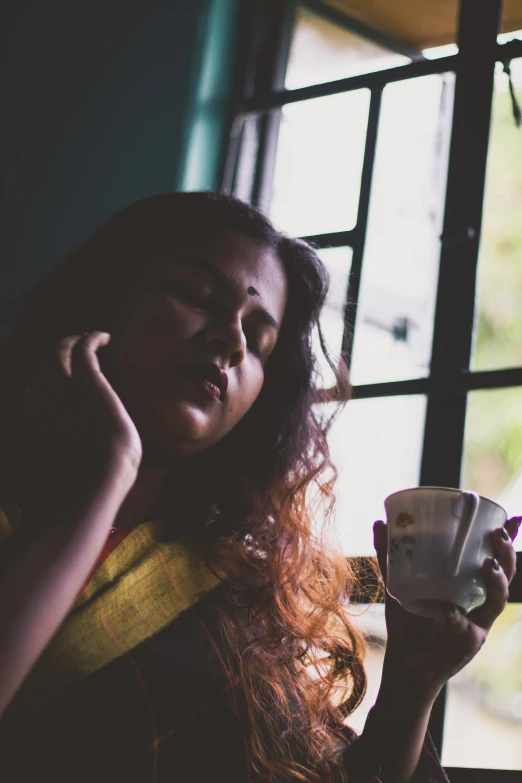 a woman holding a cup of coffee while looking out of a window