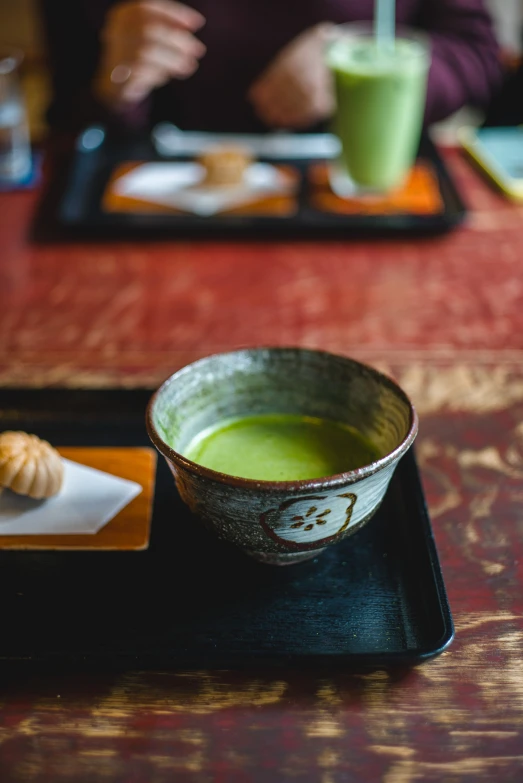 a green drink in a small bowl next to a pastry