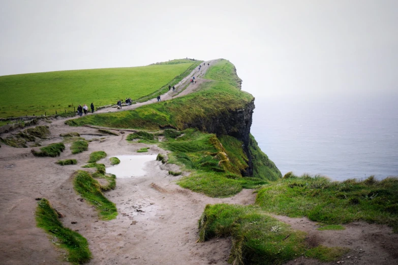 people are walking down a winding hill near the water