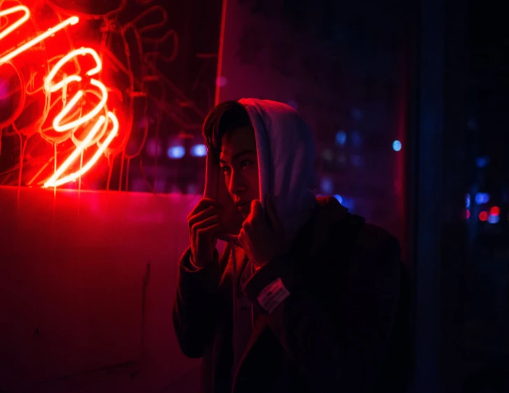 the young man is standing in front of a neon light