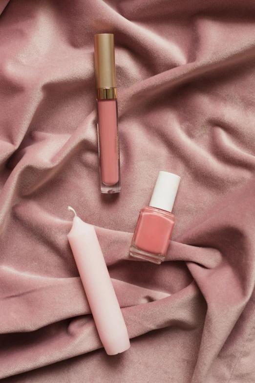 two pink nail polish bottles laying on pink fabric