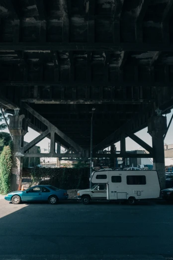an rv parked underneath a bridge with cars behind it