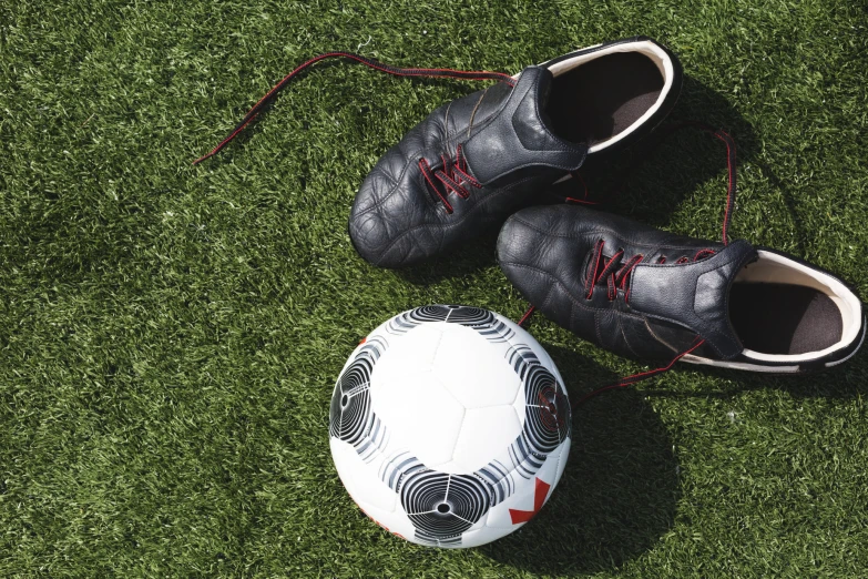 a worn up shoe on the grass beside a soccer ball