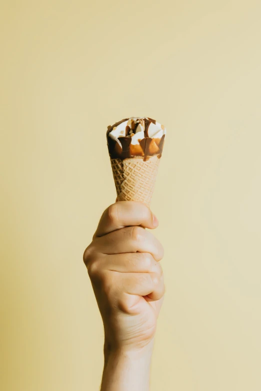 a hand holding an ice cream cone filled with small treats