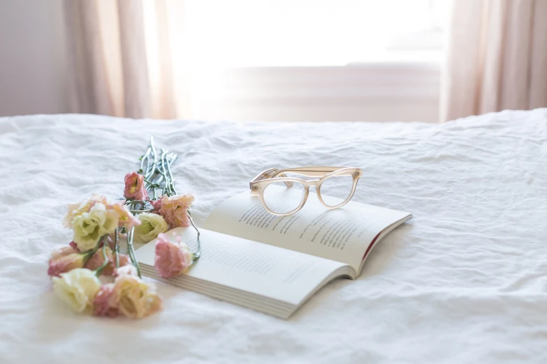 a white bed topped with two open books and a vase of flowers