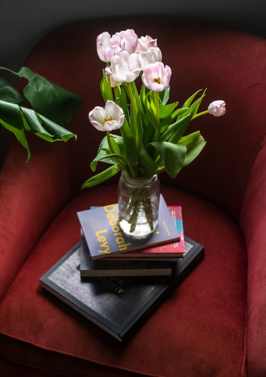 three books are stacked up on a table as a bouquet of tulips sits in front of it