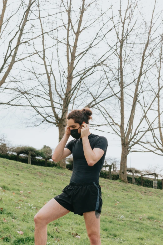 a woman in black shorts stands on a grass hill, talking on her cellphone