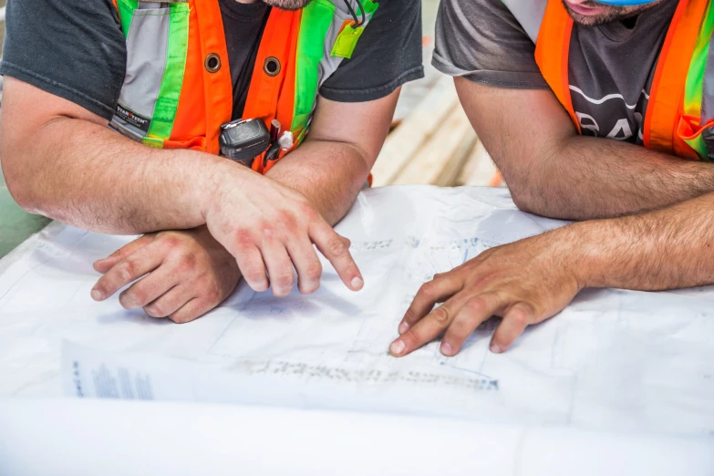 two men wearing orange safety vests are looking at blueprint