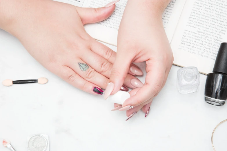 a manicured woman's hands with nail polish and an open book on top of a table