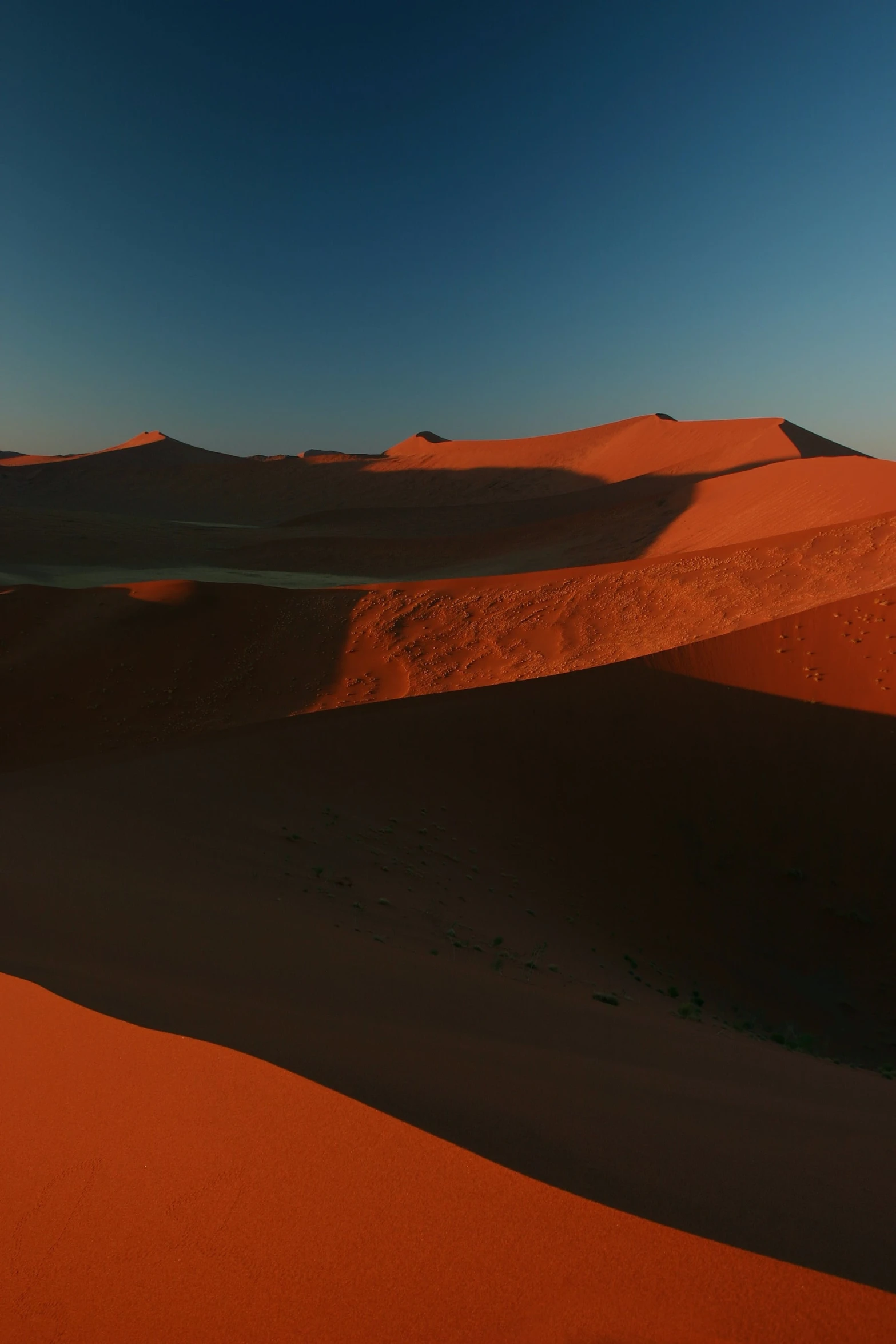 the view from the top of a desert dune, looking over some sand dunes