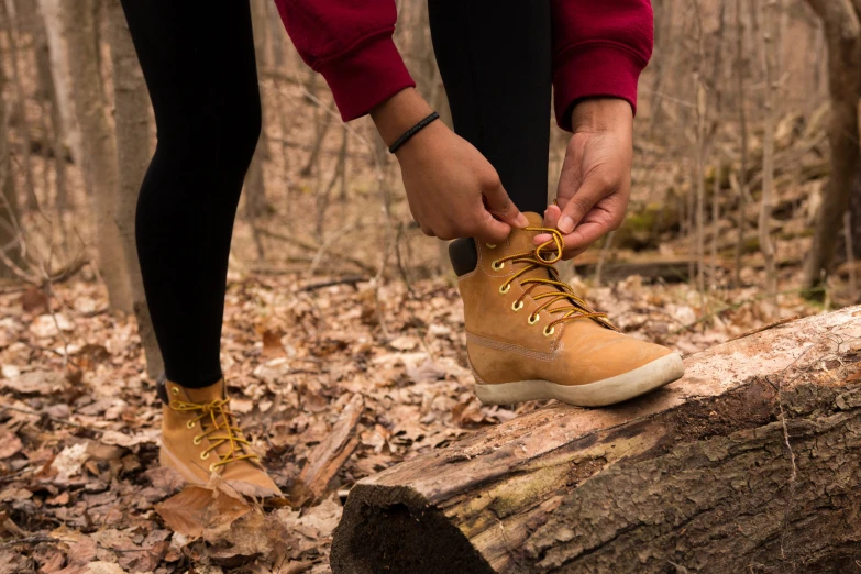 a man tying shoes with laces while walking over a log in the woods