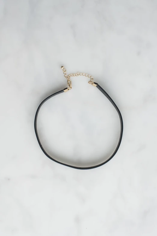 a black leather celet on white marble with a gold charm