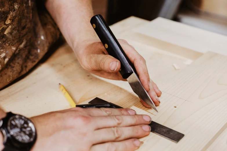 man in a watch and using a pair of scissors on a piece of wood