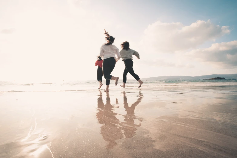 two girls run down the beach while holding their surfboards