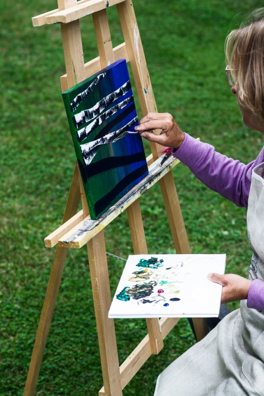 an older woman in a purple shirt painting on canvas